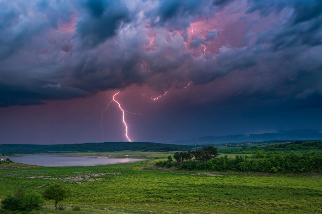 Catch the power of a lightning bolt amidst stormy skies over a lush green field.