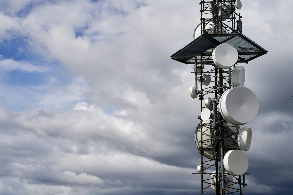 A telecommunication tower equipped with satellite dishes against a cloudy sky.